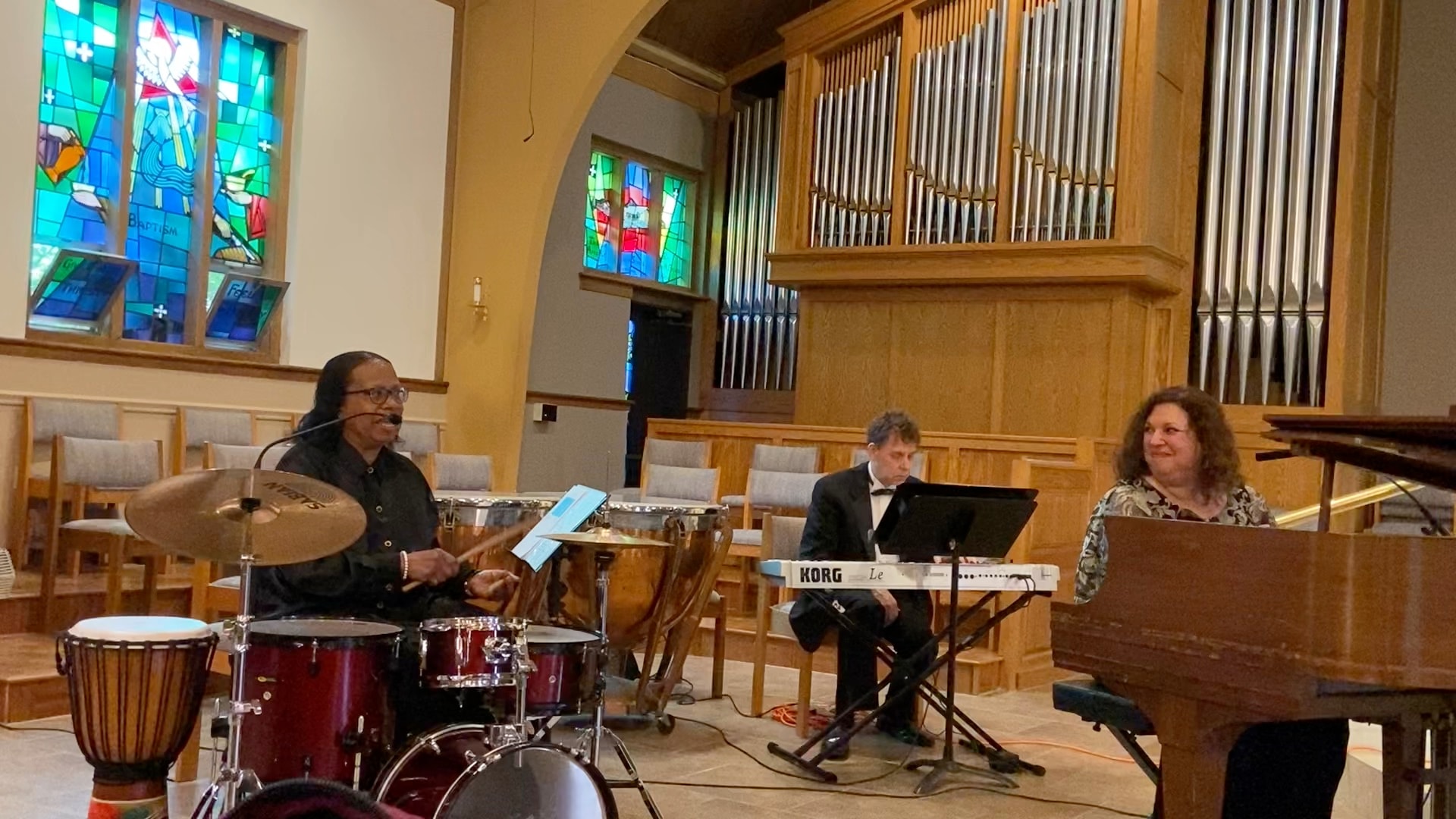 Way Past Midnight Music ensemble performing in a church — Evita on drums, a third musician on keyboard, and Melody at the piano